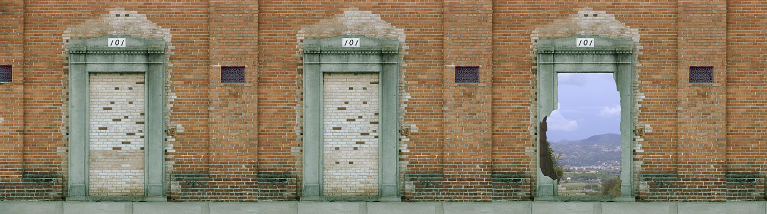A brick wall with doorways whose openings have been bricked up. Each doorway is marked 101. In one doorway the bricks have been broken out to reveal a blue sky and distant hills.