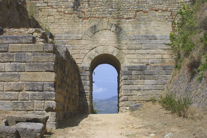 photo of an arched passageway in a stone wall, revealing a view of distant hills and sky